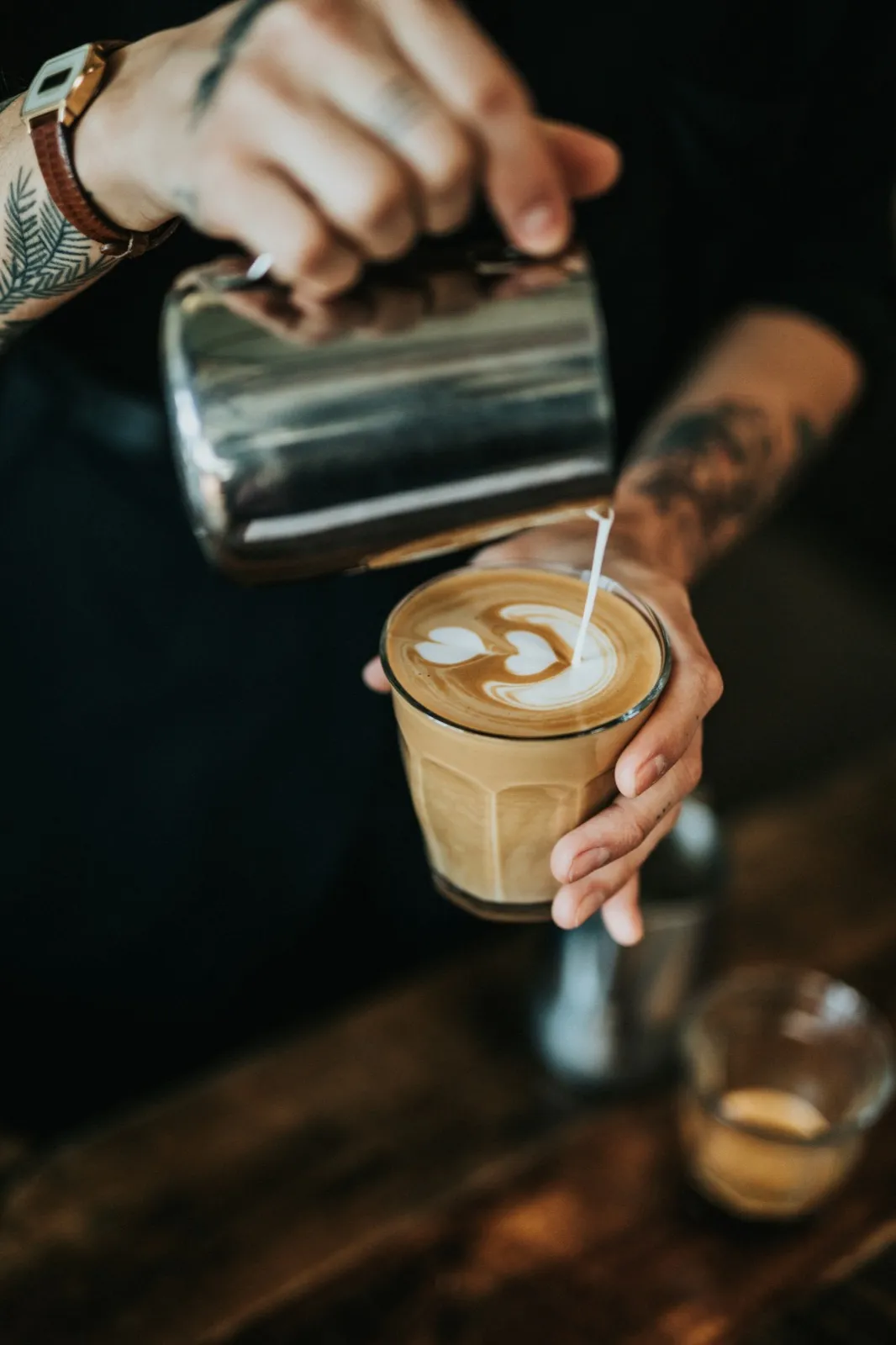 A barista pouring latte art into a glass of coffee